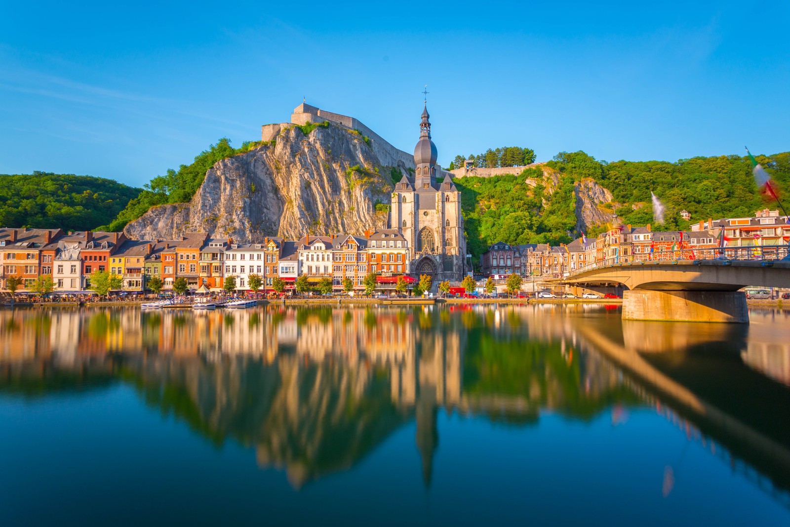 Uma vista de um rio com uma ponte e um castelo ao fundo (dinant, reflexo, água, natureza, marco)