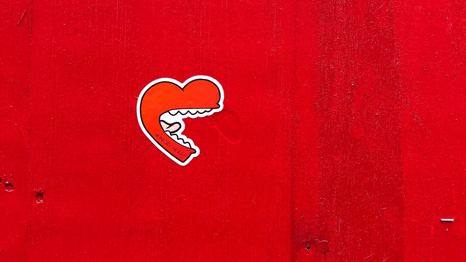 Il y a un autocollant en forme de cœur sur un mur rouge. (cœur, rouge, amour, texte, autocollant)