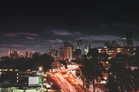 Horizonte nocturno de Melbourne: una vibrante intersección urbana con tráfico dinámico y rascacielos iluminados.