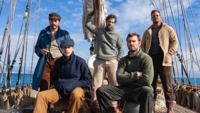 El elenco de "El Ministerio de la Guerra No Caballerosa" en un barco, mostrando camaradería y aventura contra un fondo escénico.