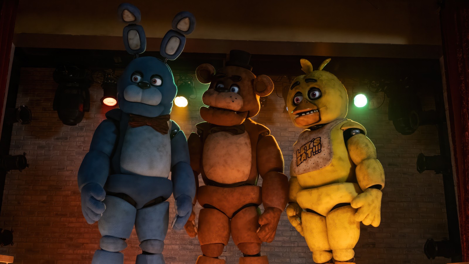 Tres animales de peluche están de pie uno al lado del otro frente a una pared de ladrillo (five nights at freddys, horror, película, fnaf, bonnie)