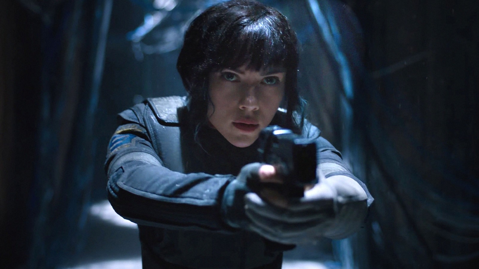 Una mujer con un atuendo negro sosteniendo un arma en una habitación oscura (ghost in the shell, scarlett johansson, paramount pictures, remolque, película)