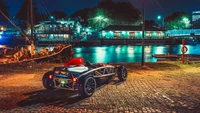 Vintage sports car parked by the water at night, illuminated by city lights.