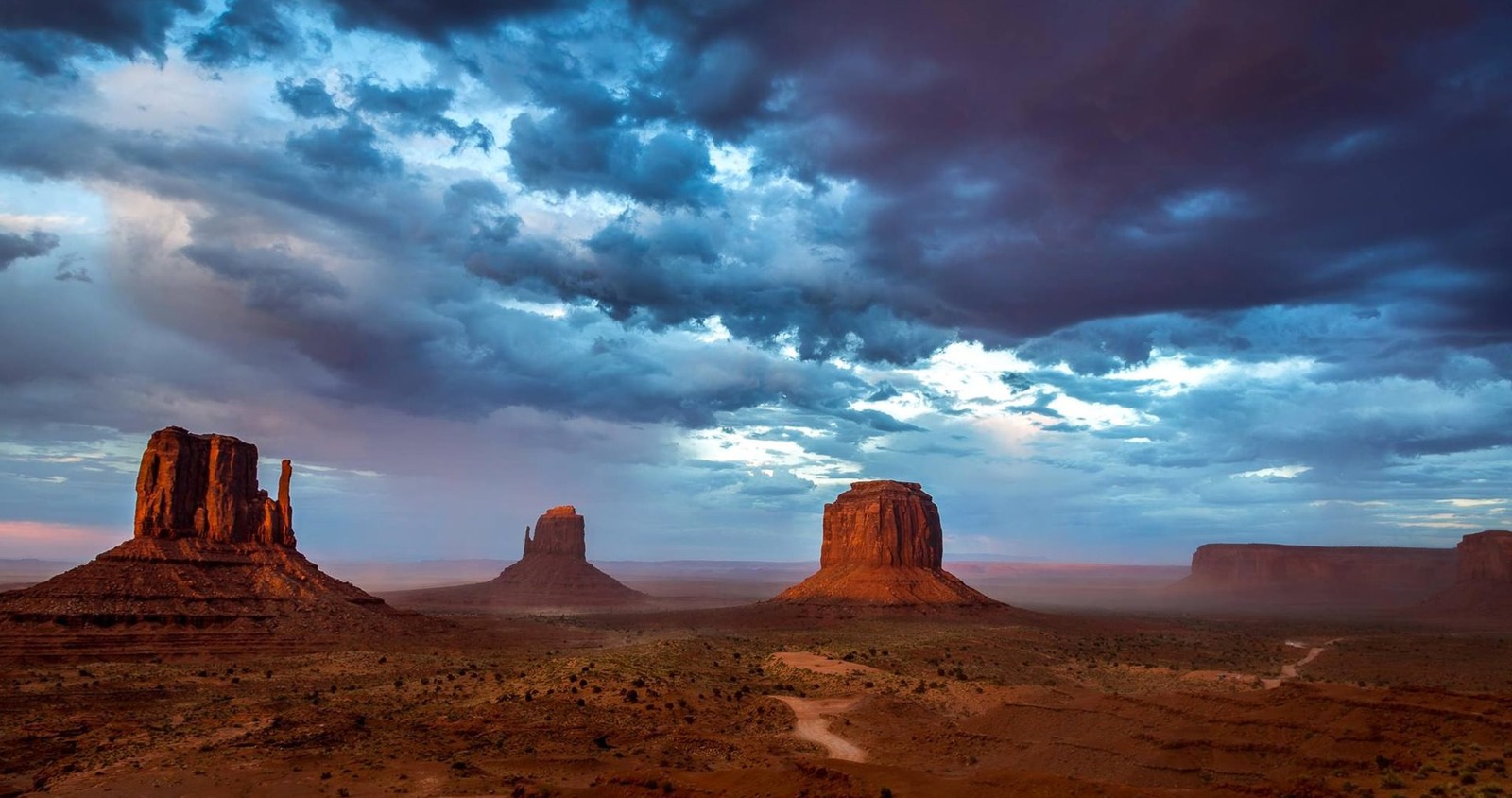 Une vue du désert avec quelques grosses pierres sous un ciel nuageux (monument valley, vallée, butte, nuage, formation)