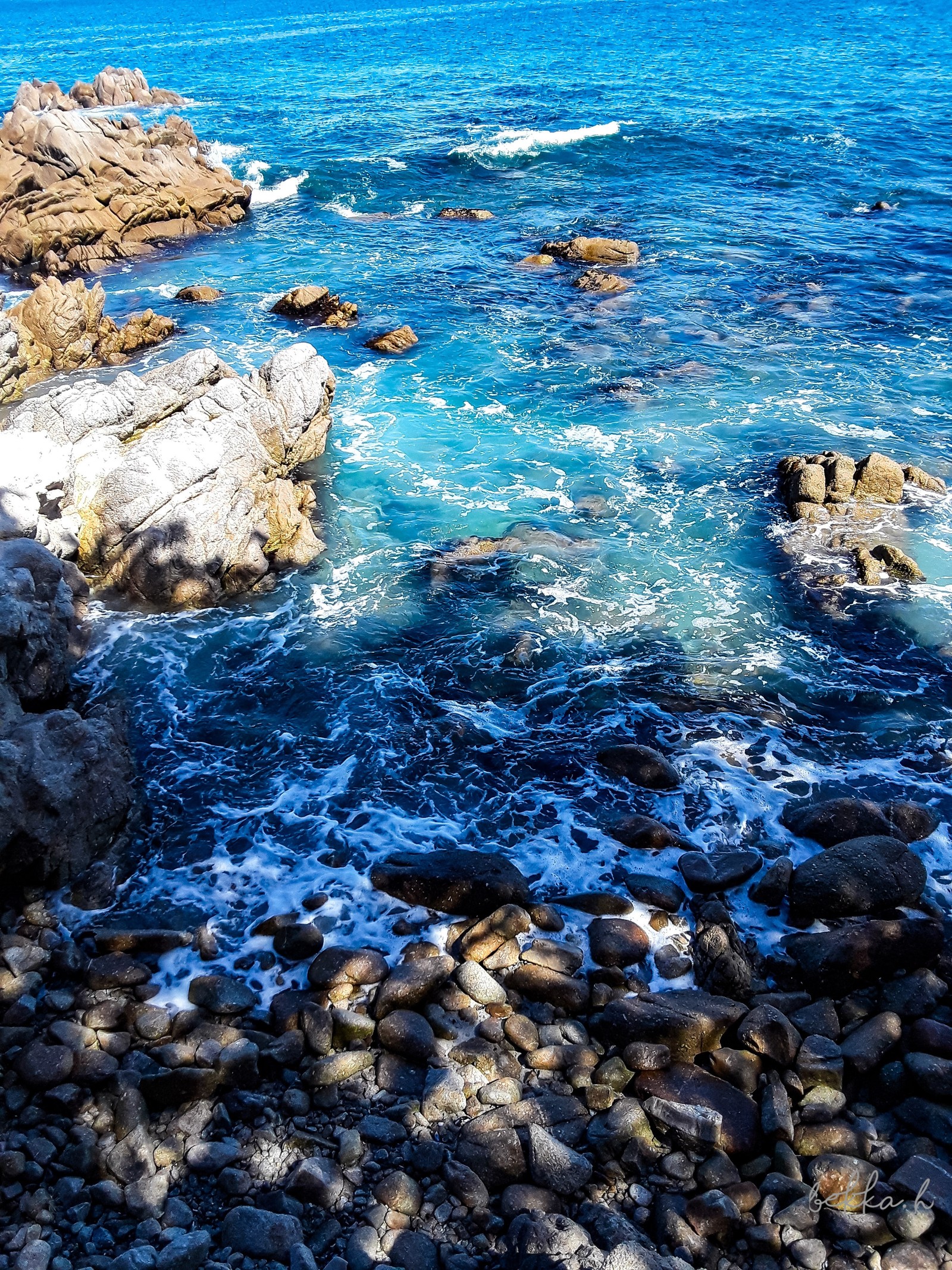 There is a person standing on a rock by the ocean (gran, more)