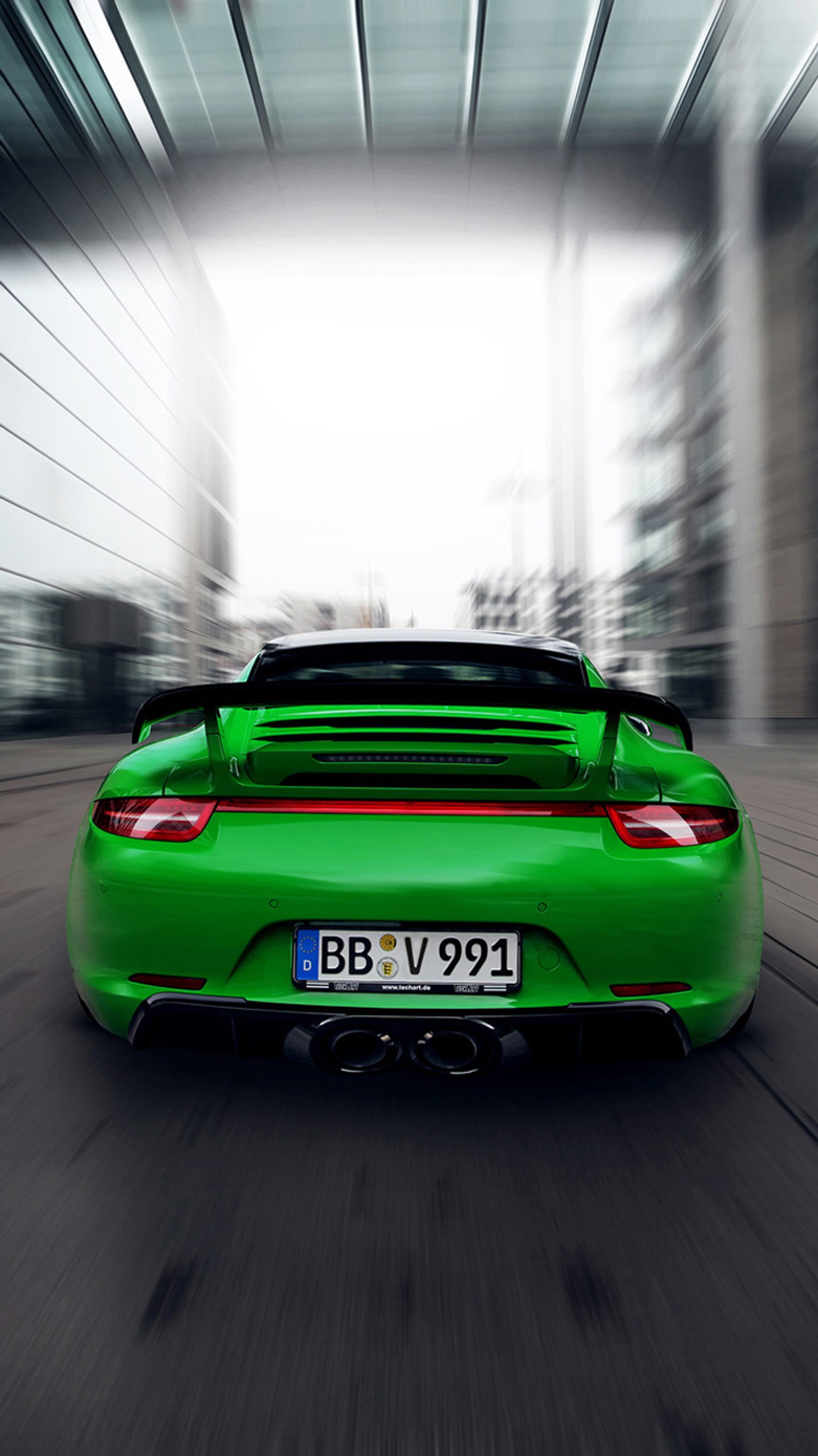 A close up of a green sports car driving down a street (city, green, iphone, porsche 911, red)