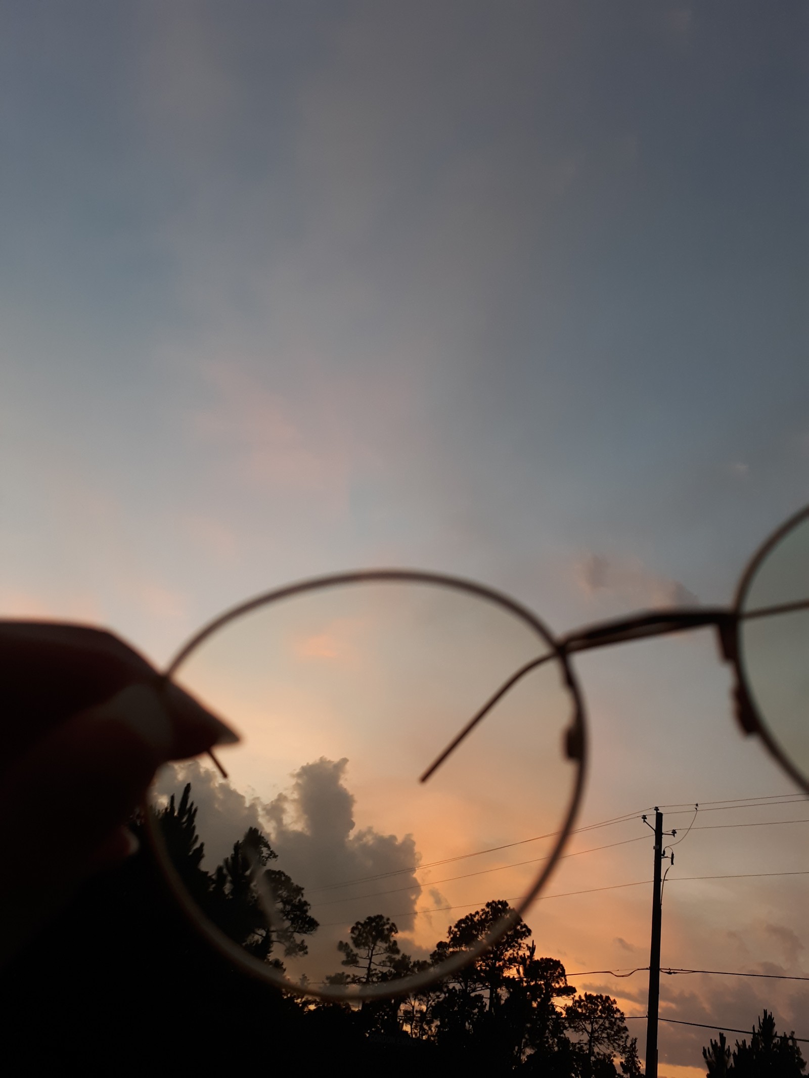 Someone holding a pair of glasses in front of a sunset (asthetic, sunset)