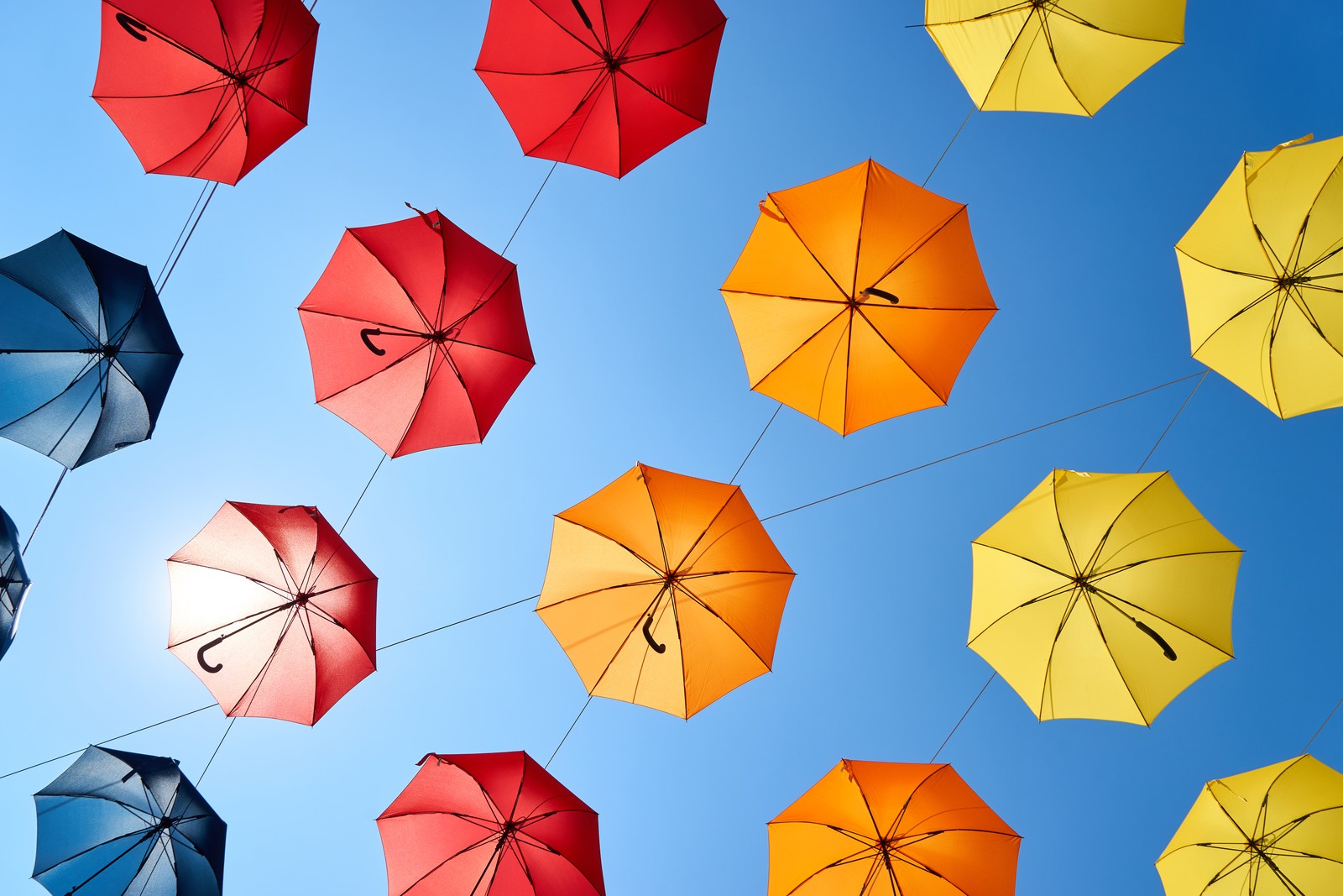 A close up of a bunch of umbrellas hanging from a wire (umbrellas, blue sky, colorful, sky view, multicolor)