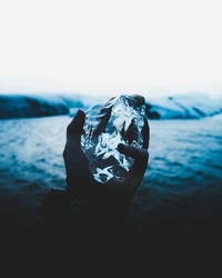 Mão segurando um pedaço de gelo glacial contra um fundo de mar turquesa