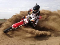 Piloto de motocross em pista de terra executando uma curva acentuada, criando uma nuvem de poeira, mostrando a emoção do esporte extremo.