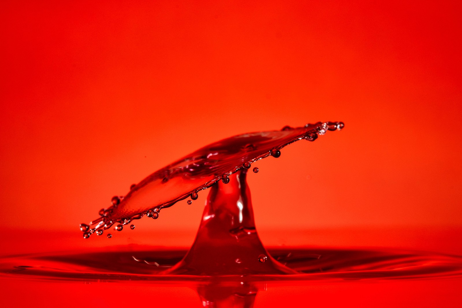 Gros plan d'une goutte de liquide rouge sur fond rouge (goutte, eau, liquide, éclaboussure, éclairage automobile)