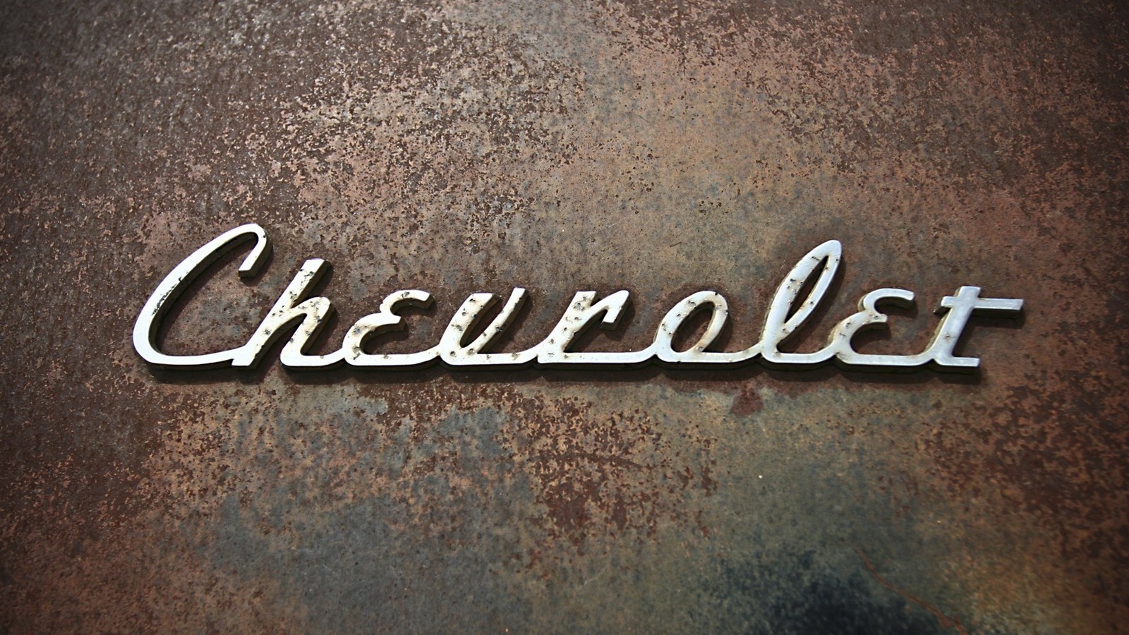 A close up of a chevrolet logo on a rusted metal surface (chevrolet, logo, text, graphics, brand)