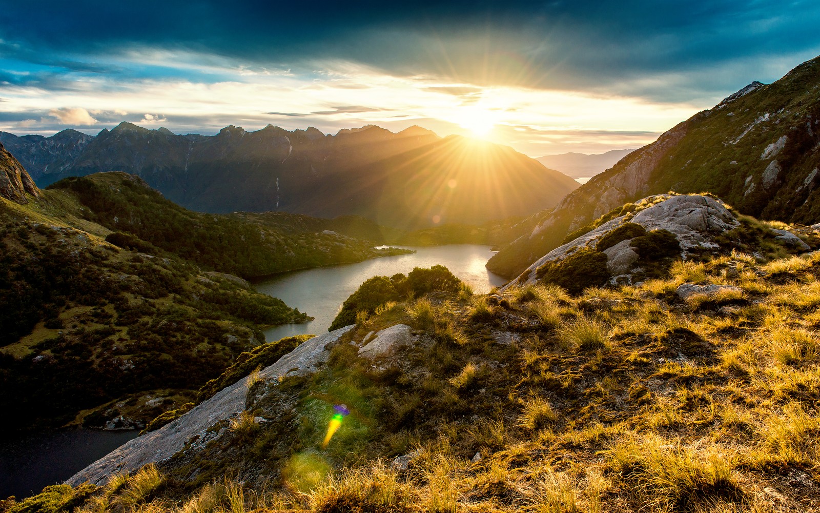 Una vista de una montaña con un lago y un sol a lo lejos (fiordland, nueva zelanda, new zealand, amanecer, vista de la montaña)