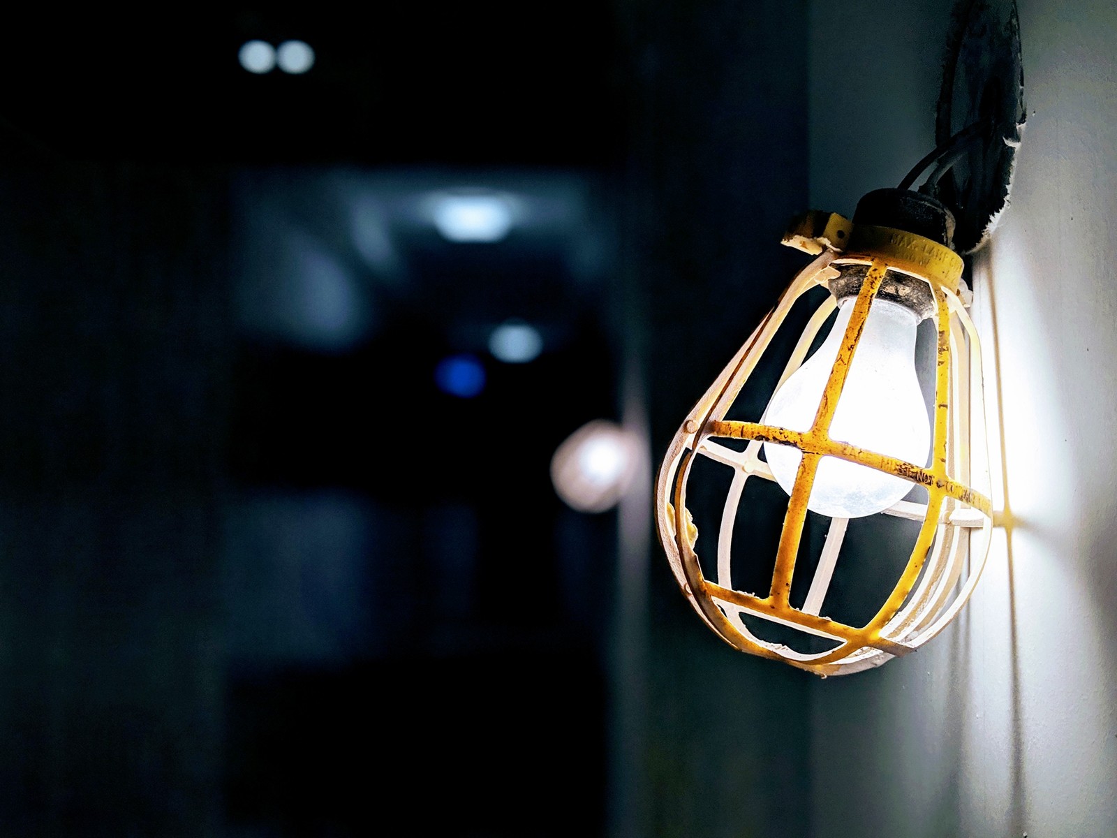 There is a light that is hanging from a wire on a wall (lighting, incandescent light bulb, lamp, yellow, light fixture)