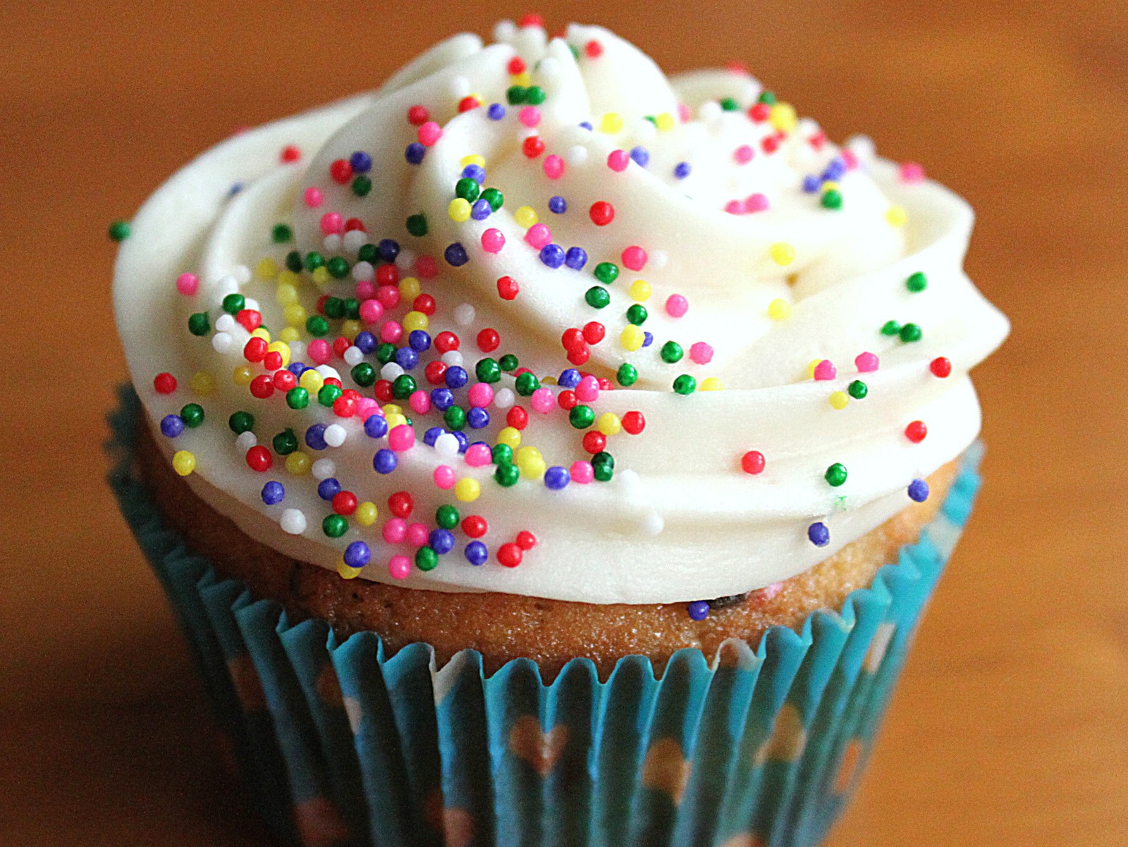 Hay un cupcake con glaseado blanco y chispas de colores (colorido, pastelito, granillo, azúcar, dulce)