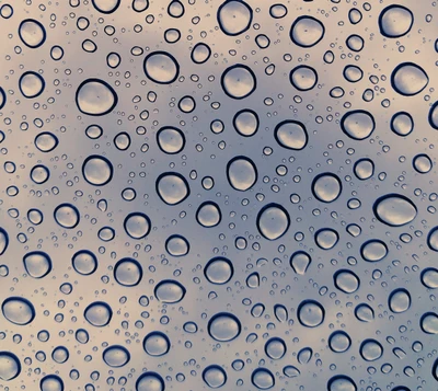 Raindrops on a windowpane, creating a textured pattern against a cloudy sky.