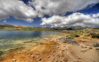 Lago de alta montaña sereno que refleja nubes y montañas dramáticas