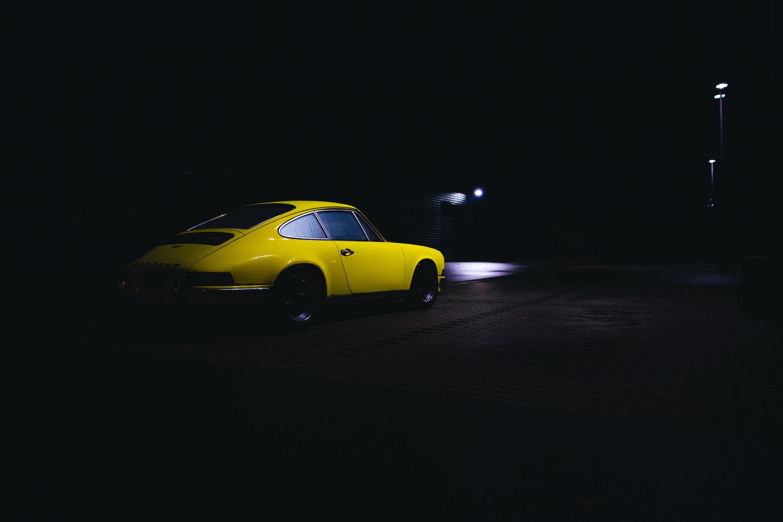 Un coche amarillo estacionado en un oscuro estacionamiento por la noche con una luz de calle (ligero, porsche, porsche 911, coche deportivo, coche compacto)