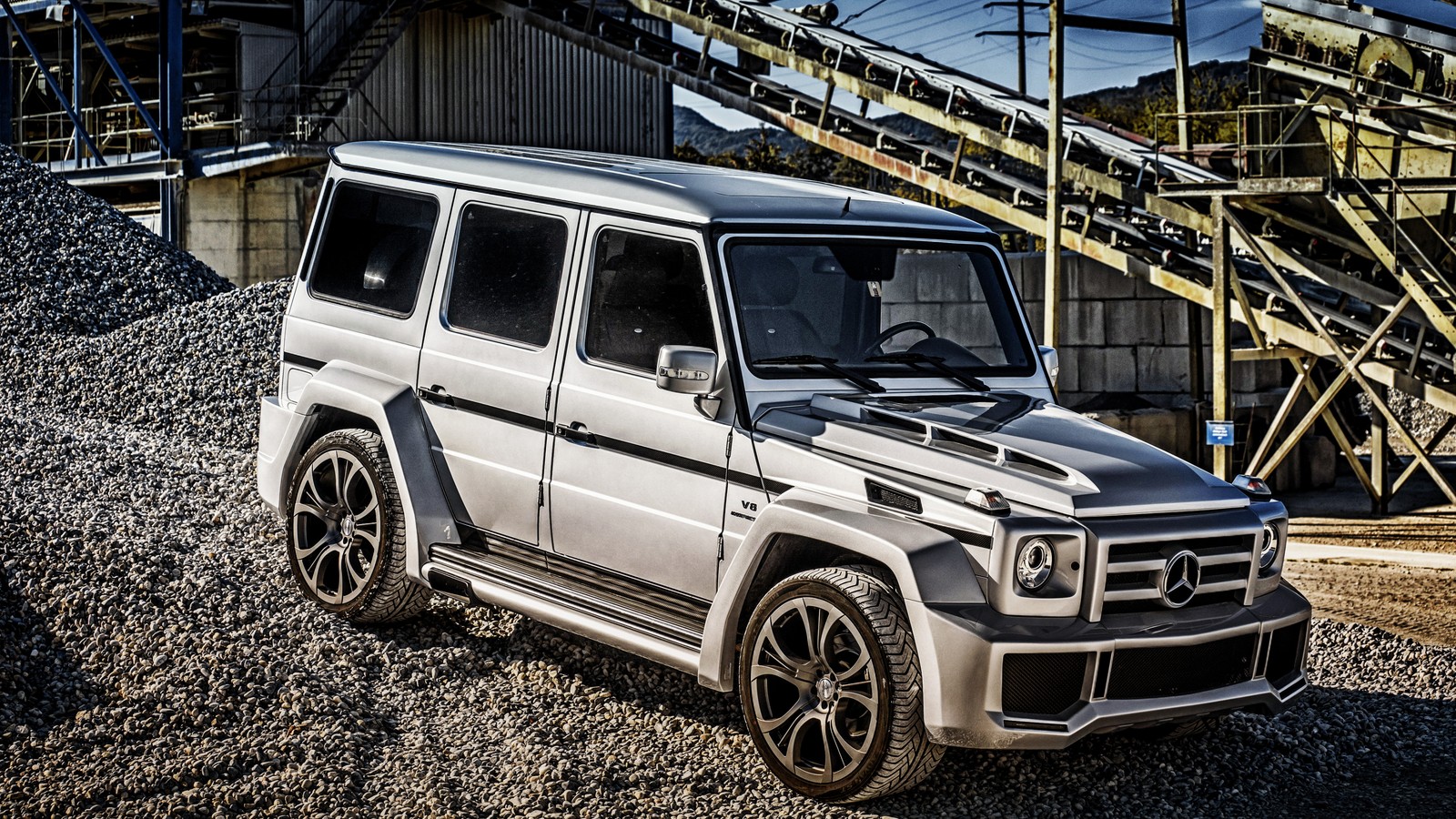 Um close em um mercedes classe g prateado estacionado em frente a um edifício (carro, brabus, pneu automotivo, roda, aro)