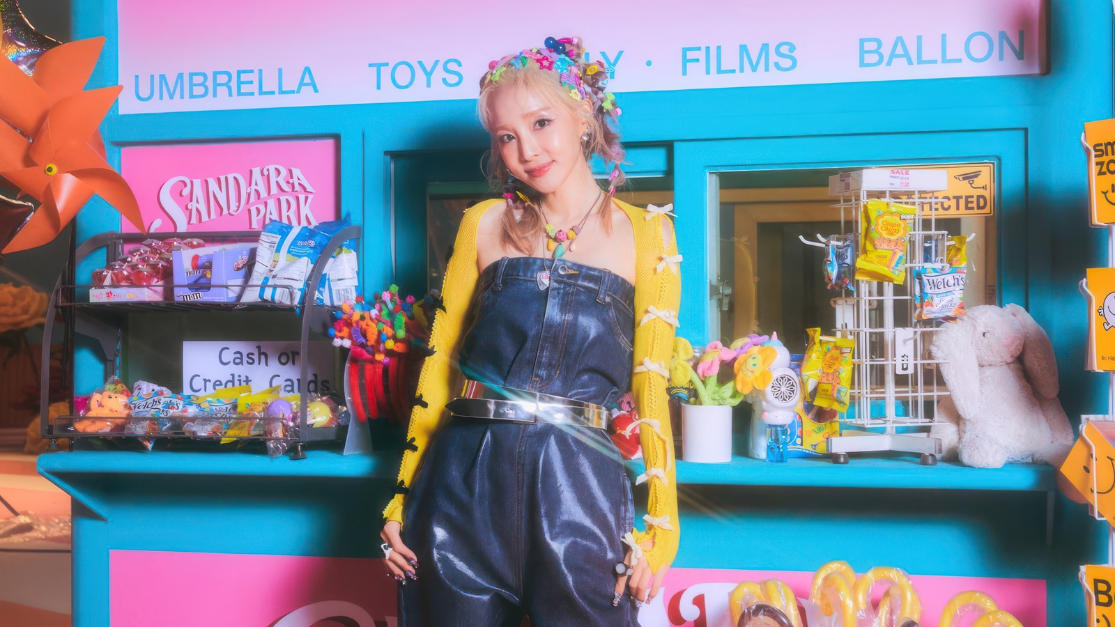 Une femme blonde en combinaison bleue debout devant une confiserie (sandara park, kpop, solo, groupe de filles coréen, korean girl group)