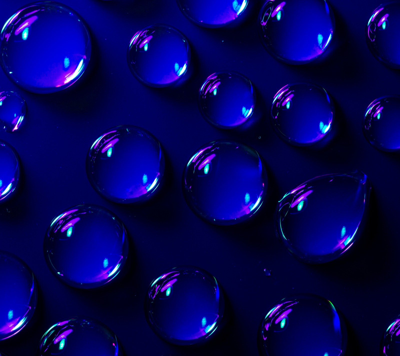 A close up of a bunch of blue glass spheres on a black surface (blue, drops, water)