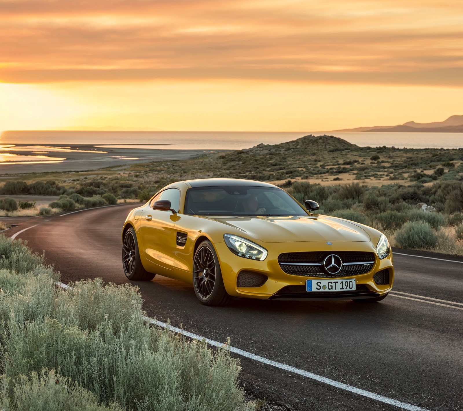 Um carro esportivo amarelo mercedes dirigindo por uma estrada perto do oceano (amg, carro, benz, mb, merc)