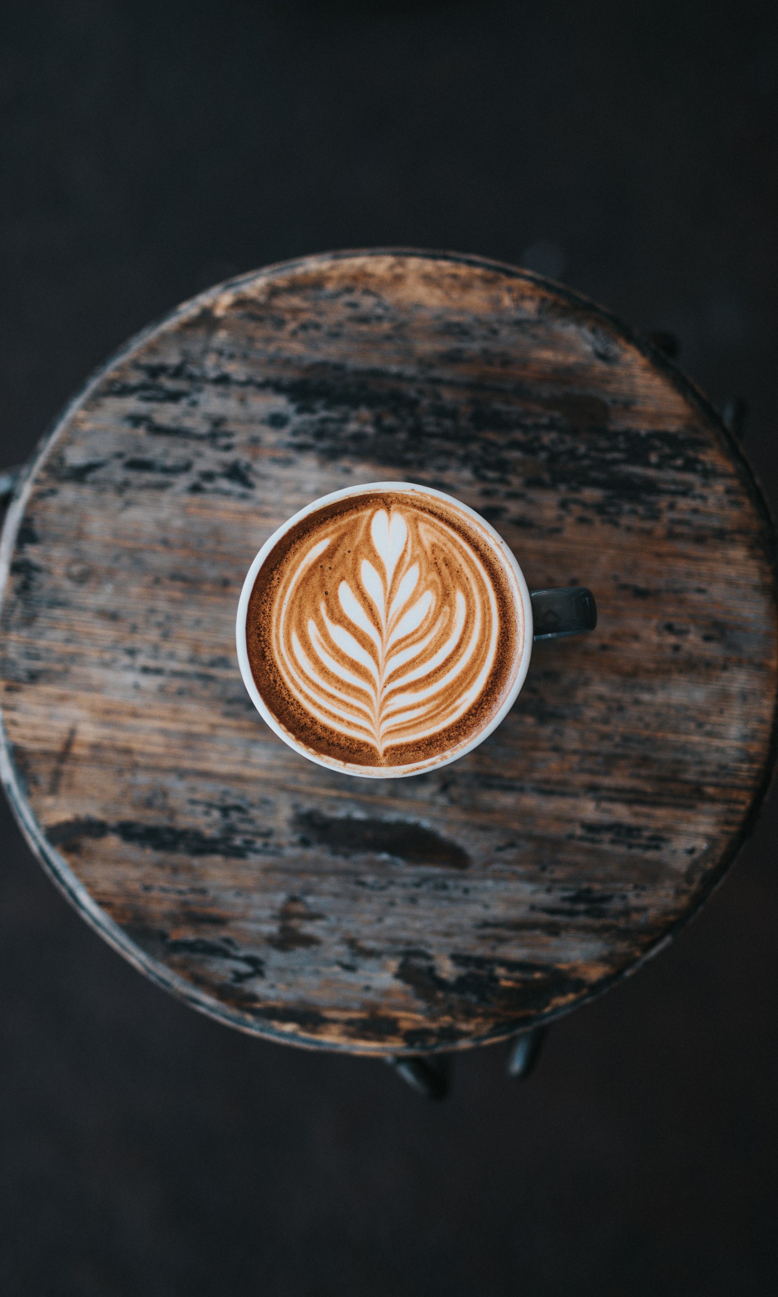 Una taza de café sobre una mesa con un patrón de hojas. (café, hora del café, taza, delicioso, latte)