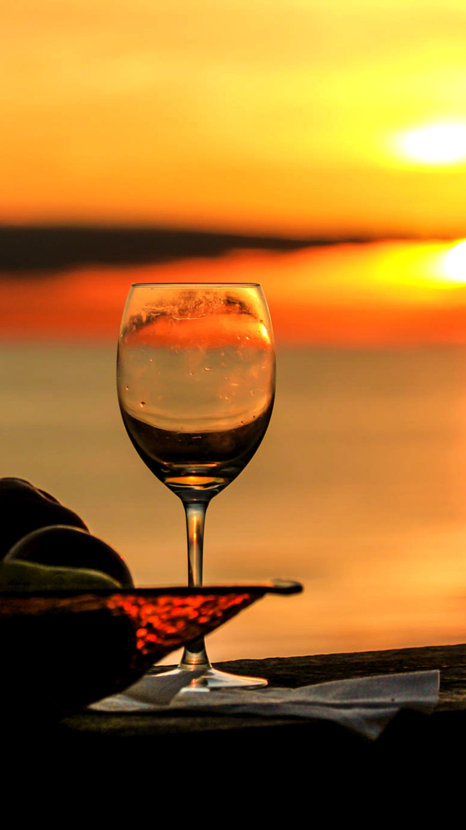 Il y a un verre de vin posé sur une table avec un coucher de soleil en arrière-plan (été, coucher de soleil, vin)