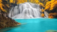 Chute d'eau sereine se déversant dans une piscine turquoise entourée de feuillage d'automne