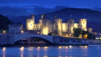 Castelo de Conwy iluminado à noite com reflexo no rio