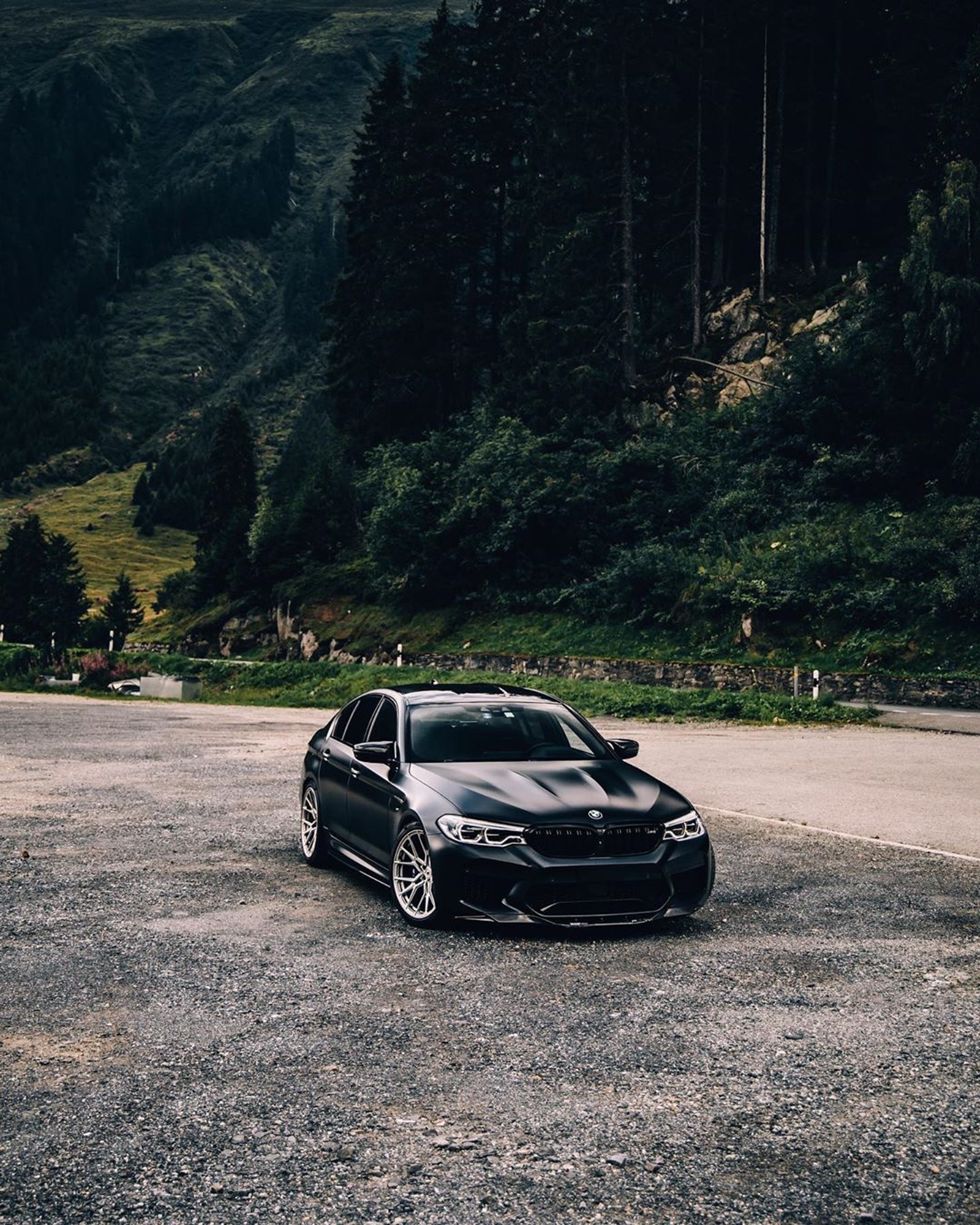 A close up of a car parked in a parking lot near a forest (black, bmw, car, competition, f90)