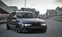 Sleek black BMW 5 Series E39 parked on an urban street, showcasing stylish rims and a personal luxury design.