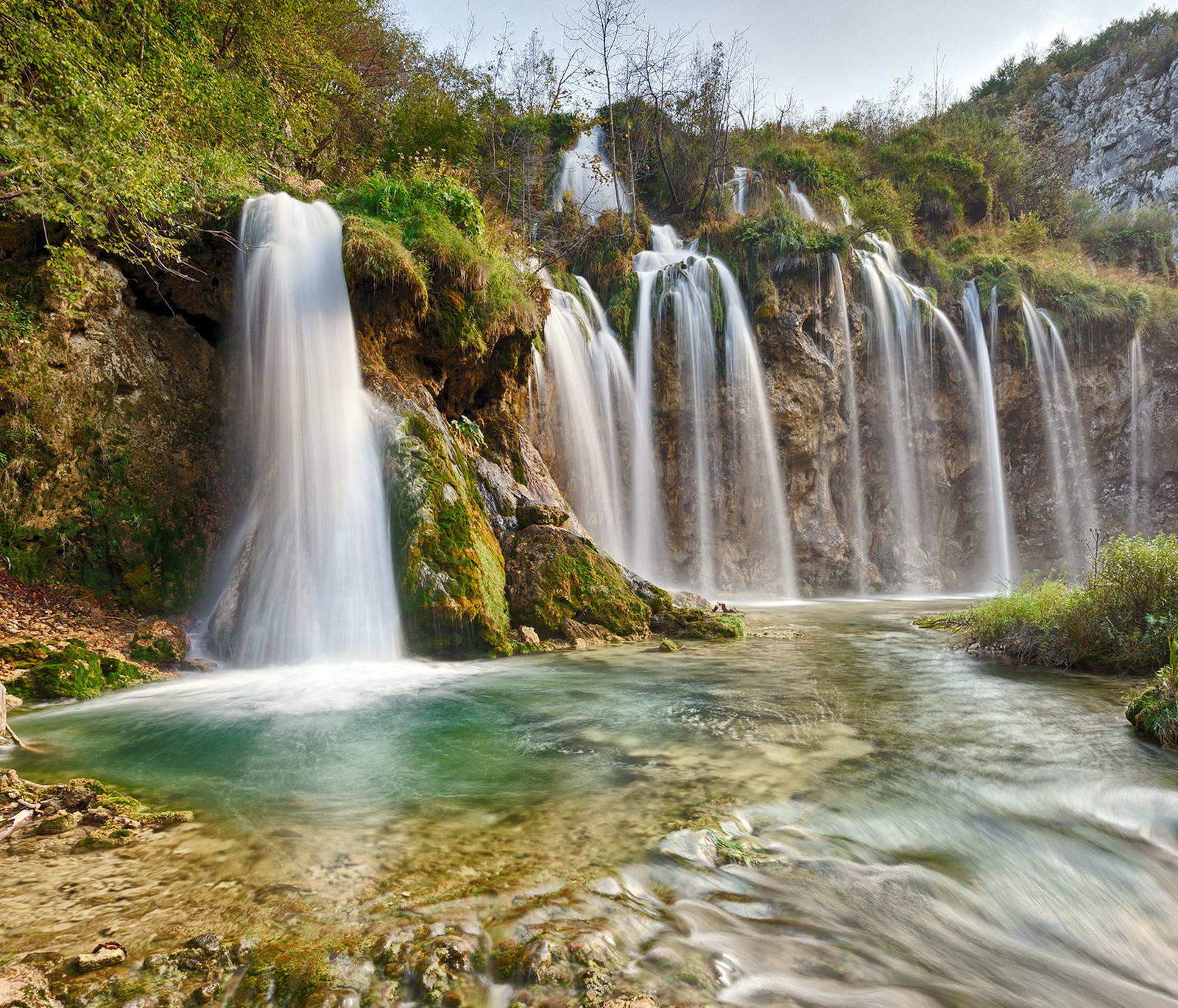 Una cascada en medio de un bosque con algunos árboles (paisaje, naturaleza, cascadas)