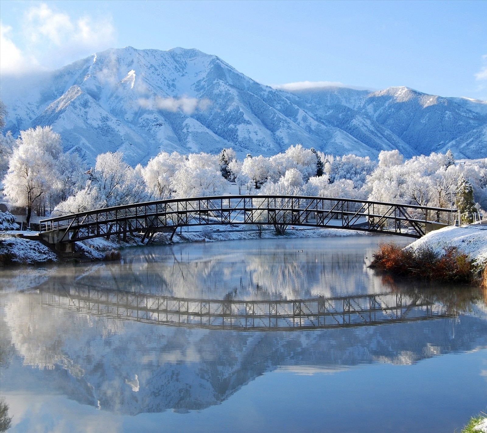 Un paysage enneigé avec un pont sur une rivière et une chaîne de montagnes (pont, enneigé)