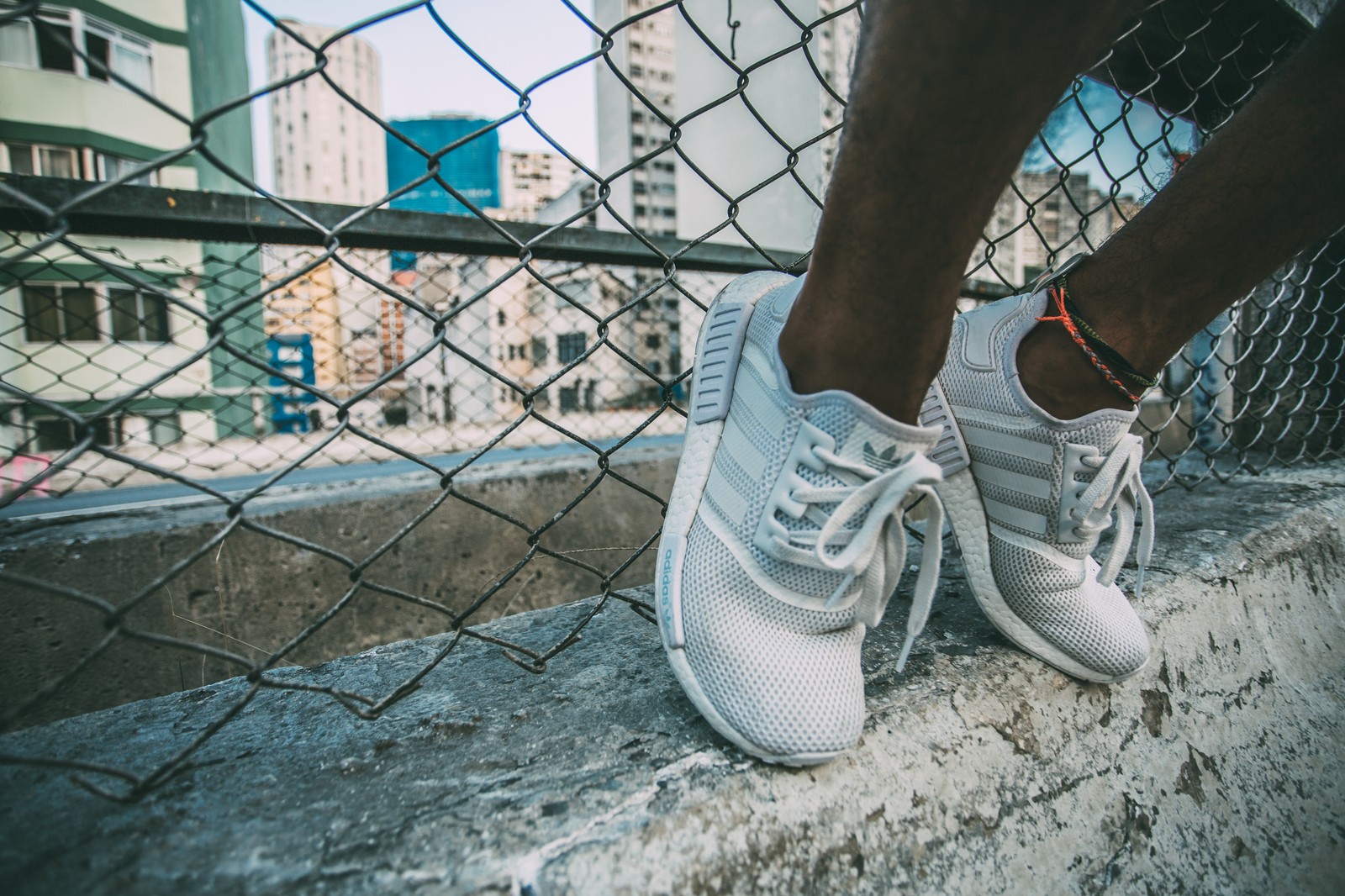 Un primer plano de los pies de una persona en un borde con una valla de cadena (zapato, zapatillas, calzado, blanco, azul)