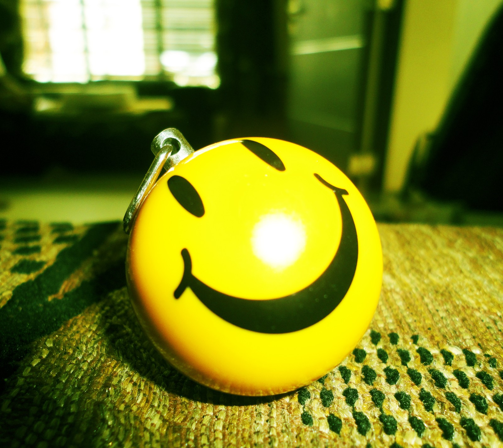 Yellow smiley face ball with black eyes on a rug (ball, smiley)