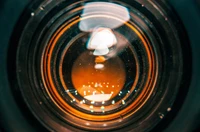 Macro view of a camera lens showcasing vibrant orange hues and intricate details, with bokeh effects and lens flare elements.