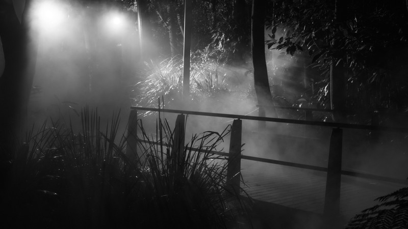 A black and white photo of a foggy park bench (water, darkness, monochrome, midnight, mist)