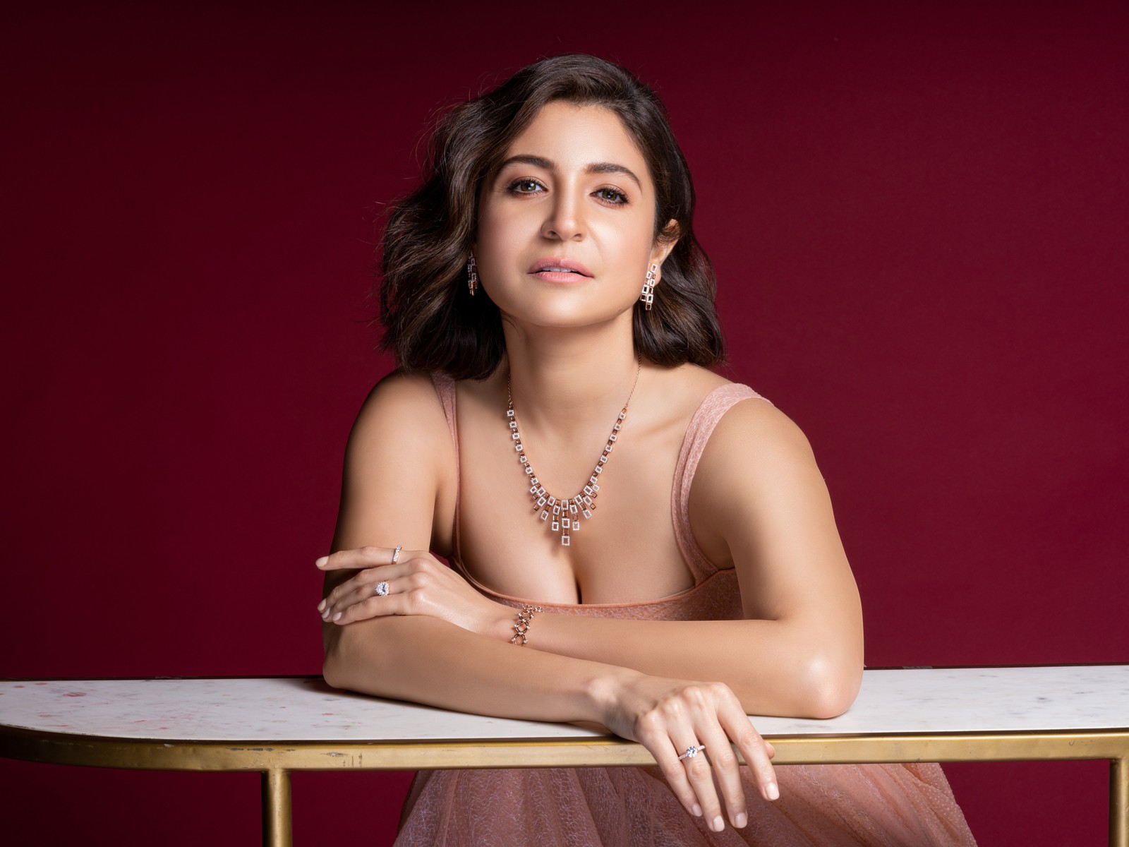 Une femme en robe rose assise à une table avec un collier (anushka sharma, actrice de bollywood, actrice indienne, 2022, 5k)