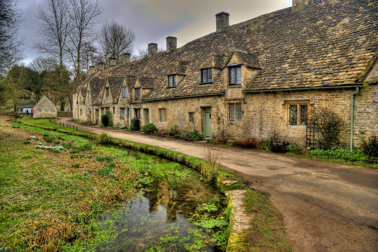 Arafed stone houses with a stream running through the middle of the road (bibury, property, house, cottage, grass)