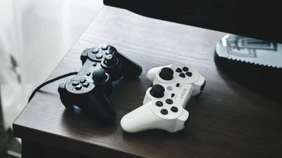 Deux manettes PlayStation : noire et blanche sur une surface en bois