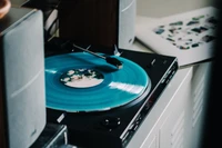 Disque phonographe turquoise jouant sur une platine avec une électronique environnante.