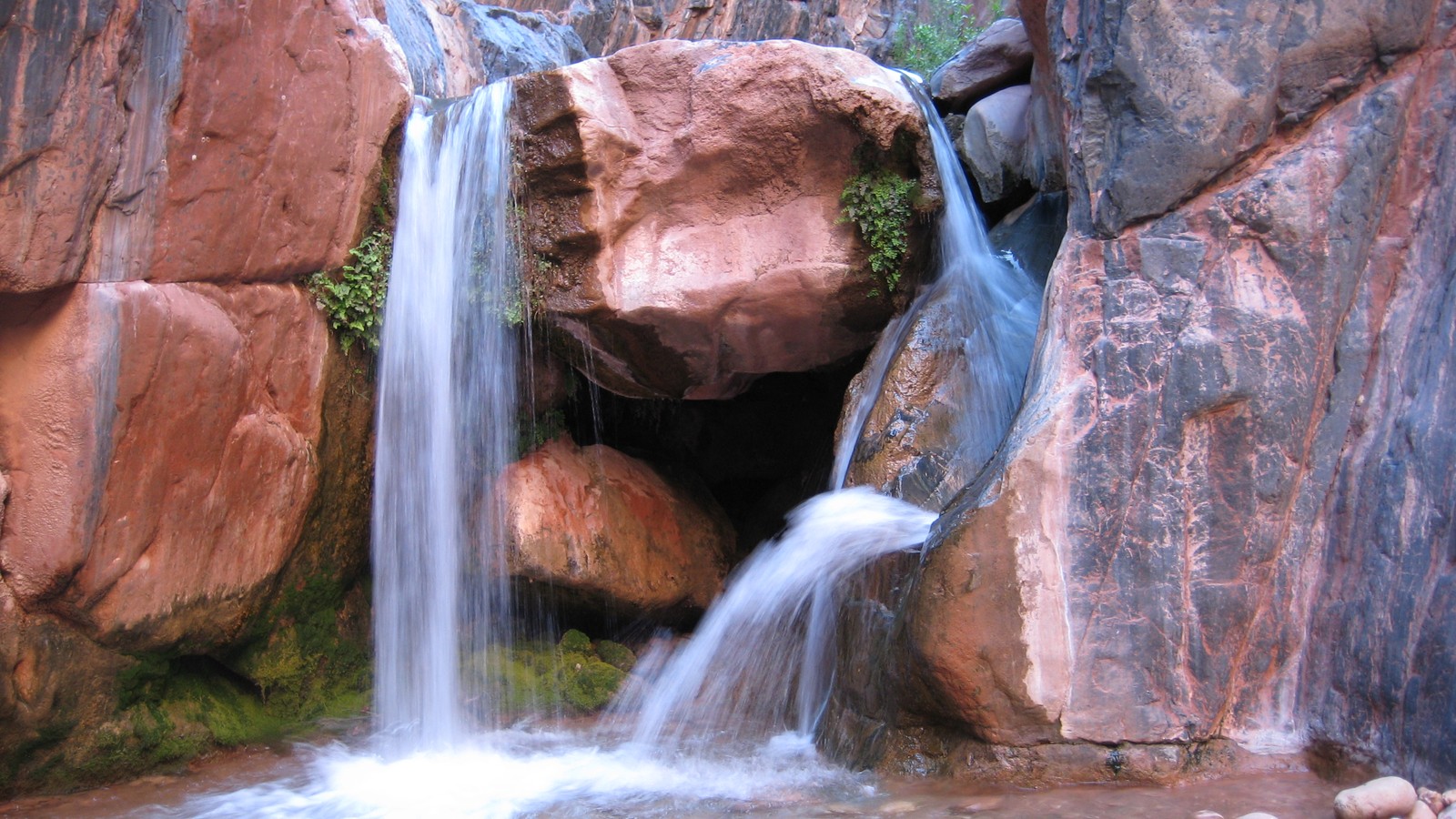 Hay una cascada que fluye sobre una formación rocosa (cascada, gran cañón, grand canyon, río colorado, recursos hídricos)