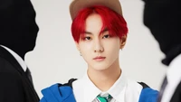 Jungwon de ENHYPEN en una pose llamativa, mostrando un cabello rojo audaz y un atuendo urbano elegante contra un fondo minimalista.