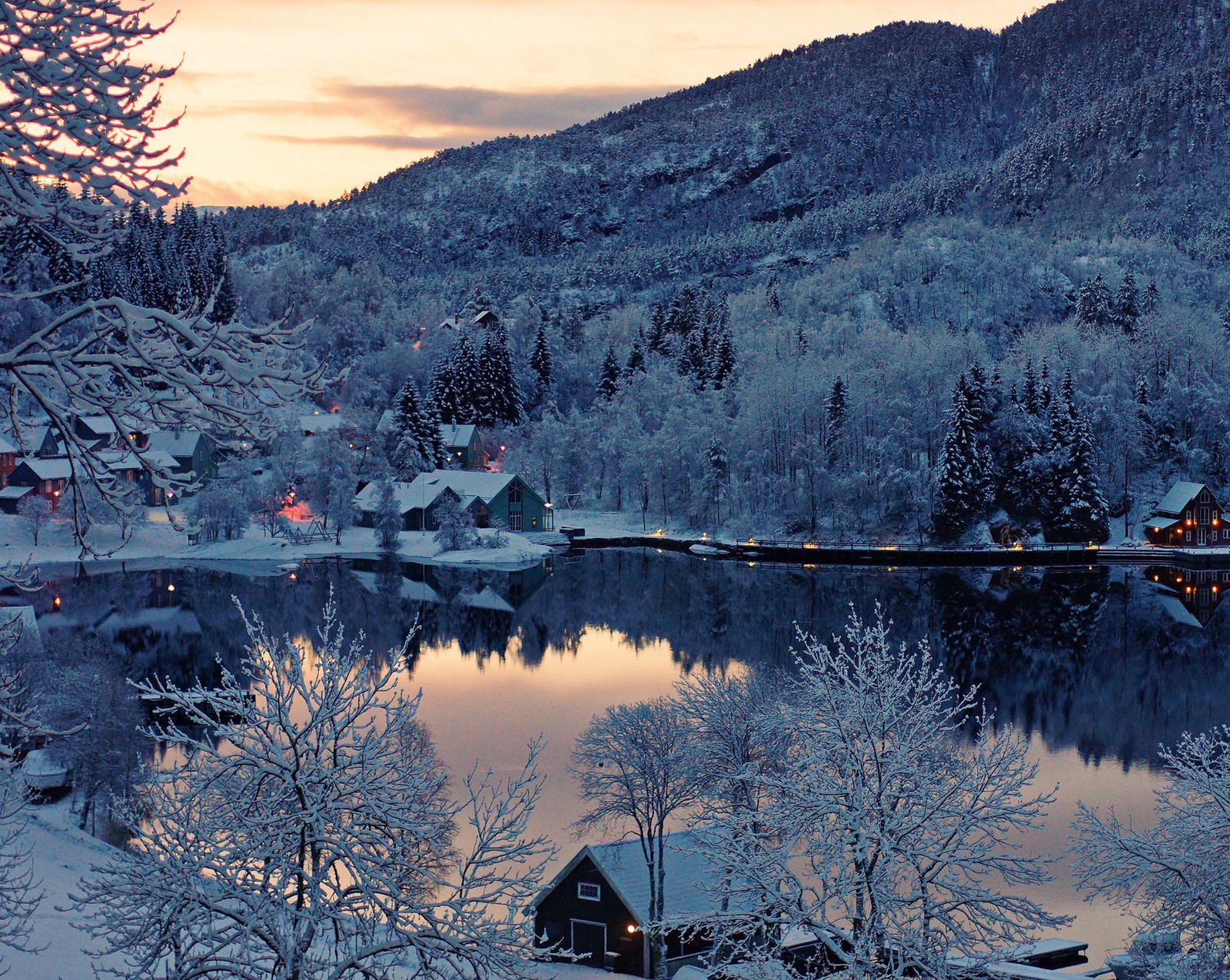 Cena nevada de uma pequena aldeia com um lago e uma montanha ao fundo (lago, inverno)