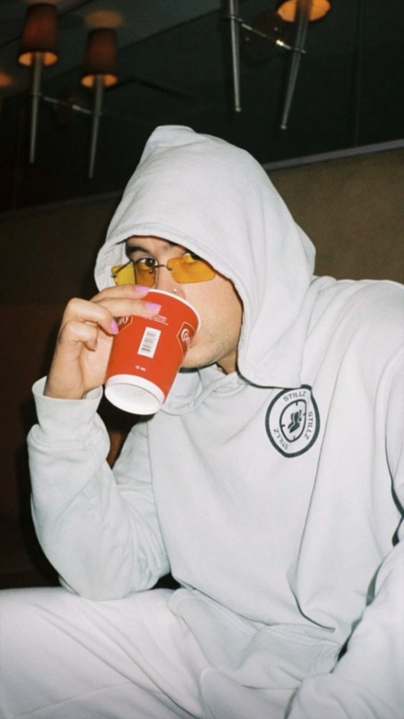 Há um homem com um moletom branco bebendo uma xícara de café (bad bunny, el conejo malo)