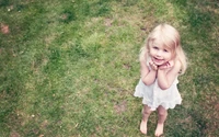 A joyful girl in a white dress stands barefoot on a lush green lawn, embodying innocence and wonder.