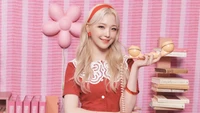 Baek Ji Heon de fromis_9 pose joyeusement avec un téléphone vintage sur un fond rose ludique, incarnant une esthétique K-pop vibrante.