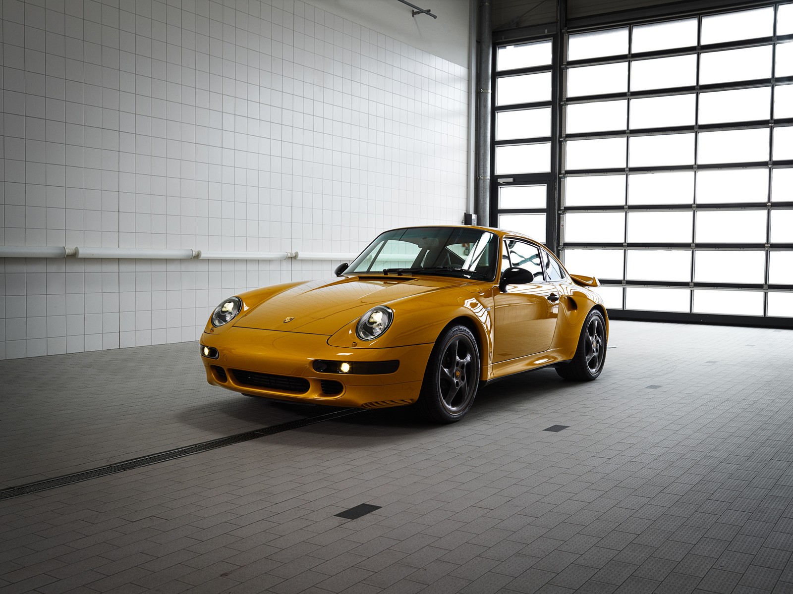 Arafed yellow sports car parked in a garage with a large window (porsche, porsche 911, porsche 930, car, sports car)