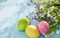 Bunte Ostereier, umgeben von zarten Frühlingsblumen auf einer pastellblauen Oberfläche.